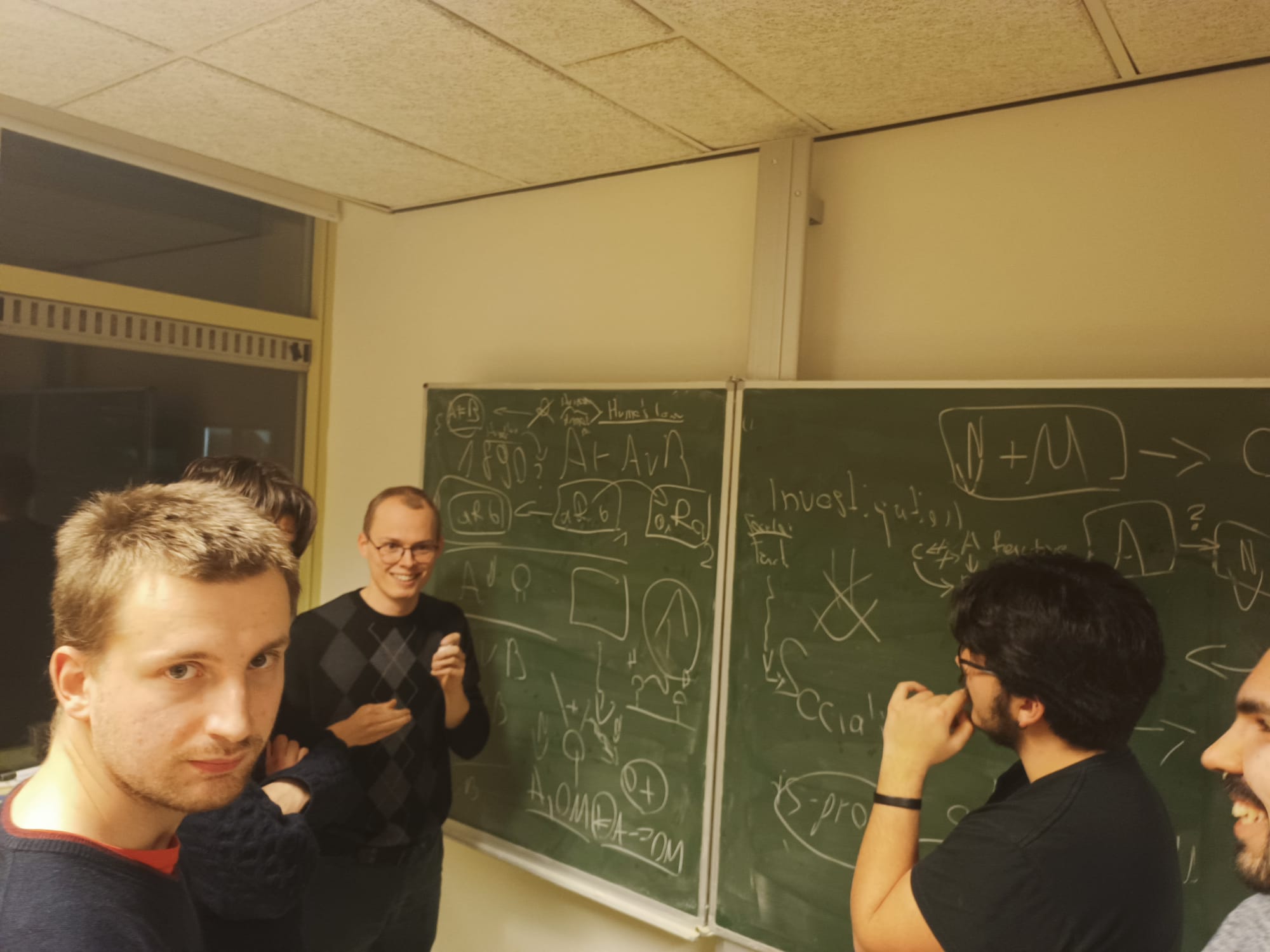 Férreol, Giacomo, Lorenz, Orestis, and Blaž discussing in front of a blackboard with logical formulas on it